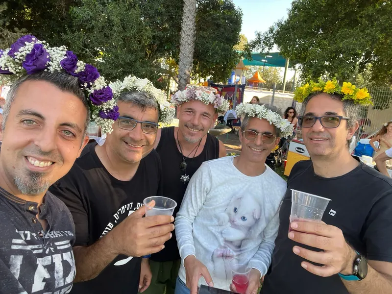 חברי הלהקה עם זרי פרחים על הראש, מרימים כוסית באירוע